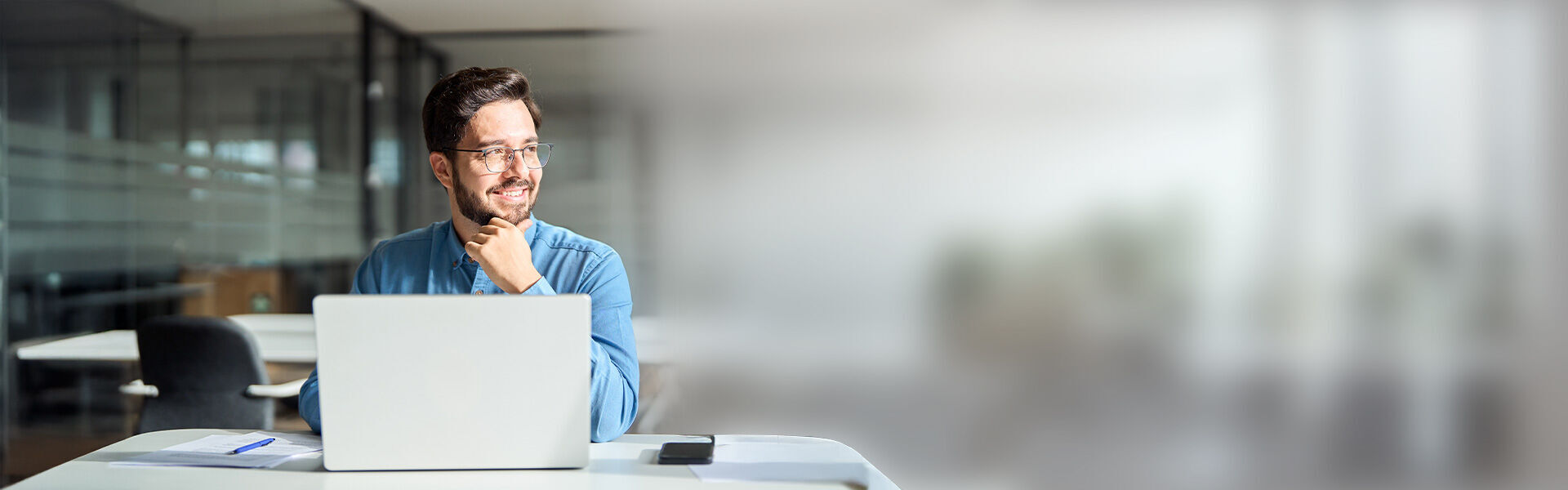 ein Mann sitzt an einem Schreibtisch mit einem Laptop, daneben eine Sprechblase