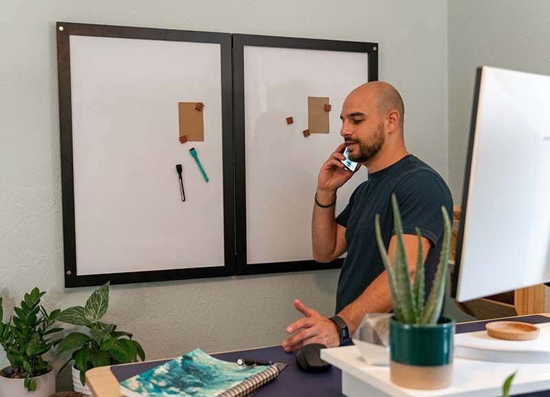 Ein Speditionskaufmann steht telefonierend neben seinem Schreibtisch vor einem Whiteboard.